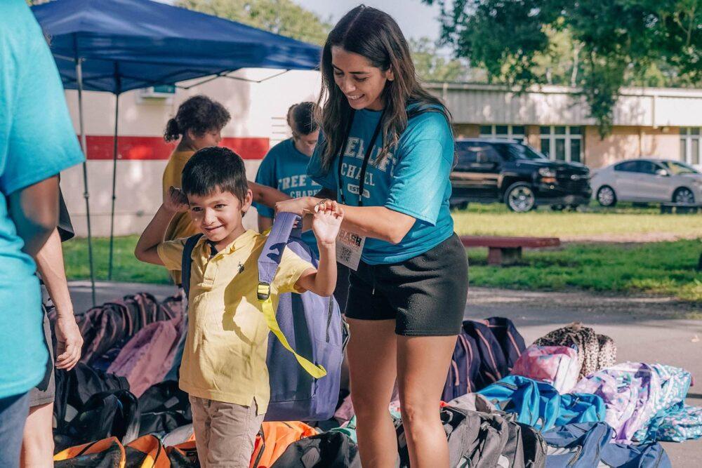Free Life Chapel volunteer serving at Back to School Bash, giving a backpack to a child in need